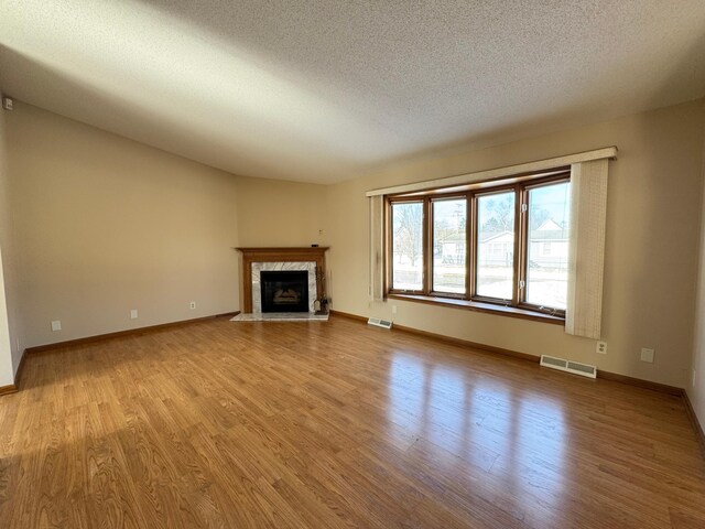 unfurnished living room featuring visible vents, a textured ceiling, a premium fireplace, and wood finished floors