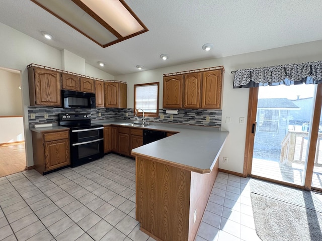 kitchen featuring lofted ceiling, brown cabinets, a peninsula, black appliances, and a sink