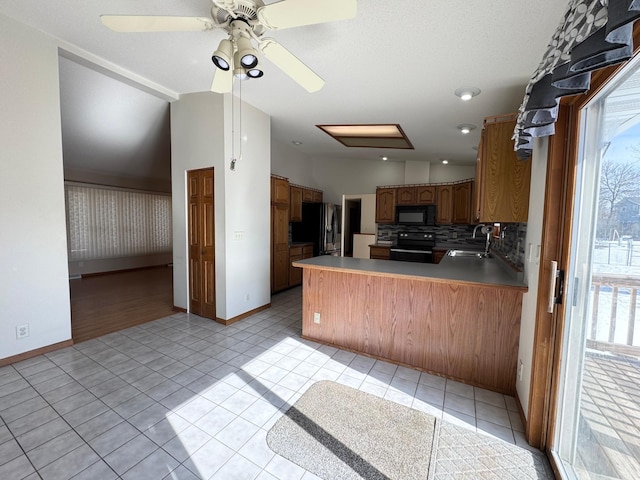 kitchen with light tile patterned floors, decorative backsplash, a healthy amount of sunlight, a peninsula, and black appliances