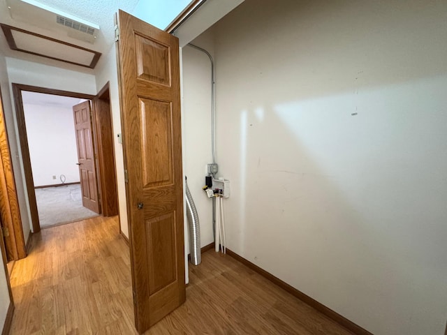 hallway with visible vents, light wood-style flooring, and baseboards