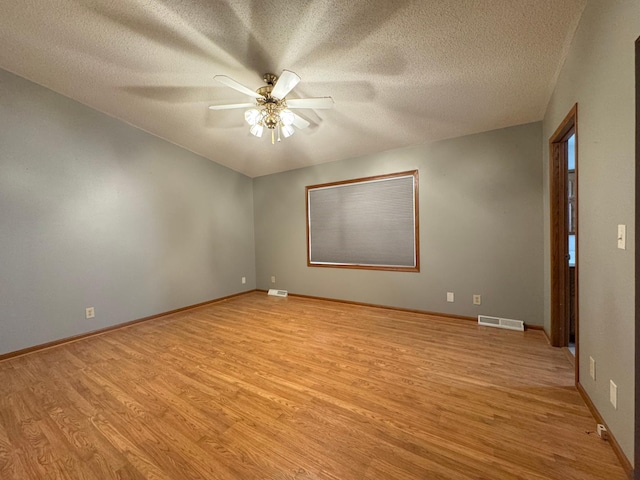 empty room featuring visible vents, light wood-style flooring, ceiling fan, a textured ceiling, and baseboards