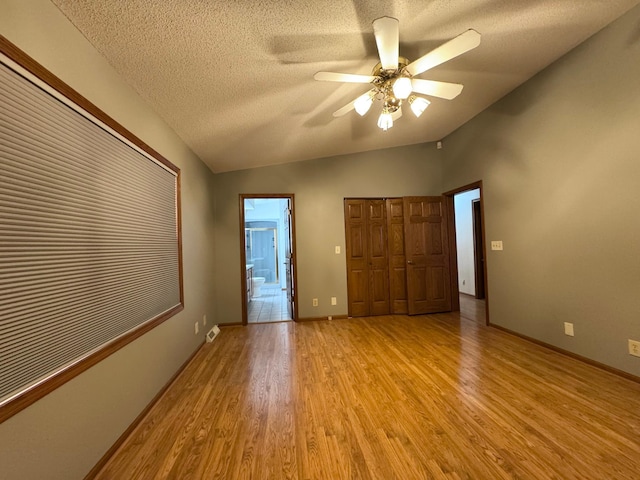 unfurnished bedroom with lofted ceiling, a textured ceiling, baseboards, a closet, and light wood-type flooring