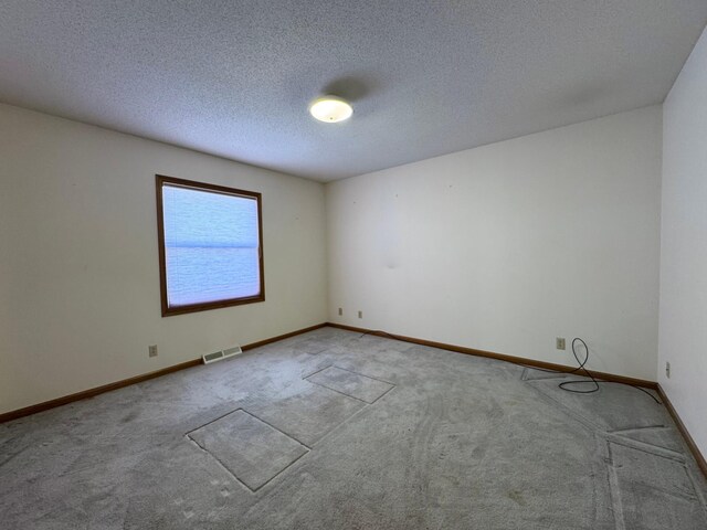 carpeted spare room with a textured ceiling, visible vents, and baseboards