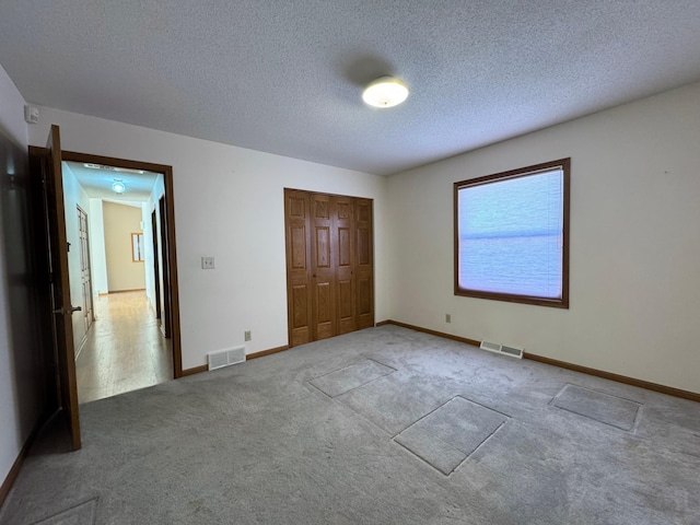 unfurnished bedroom featuring carpet floors, a textured ceiling, visible vents, and a closet