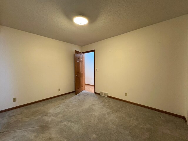 carpeted empty room with a textured ceiling, visible vents, and baseboards