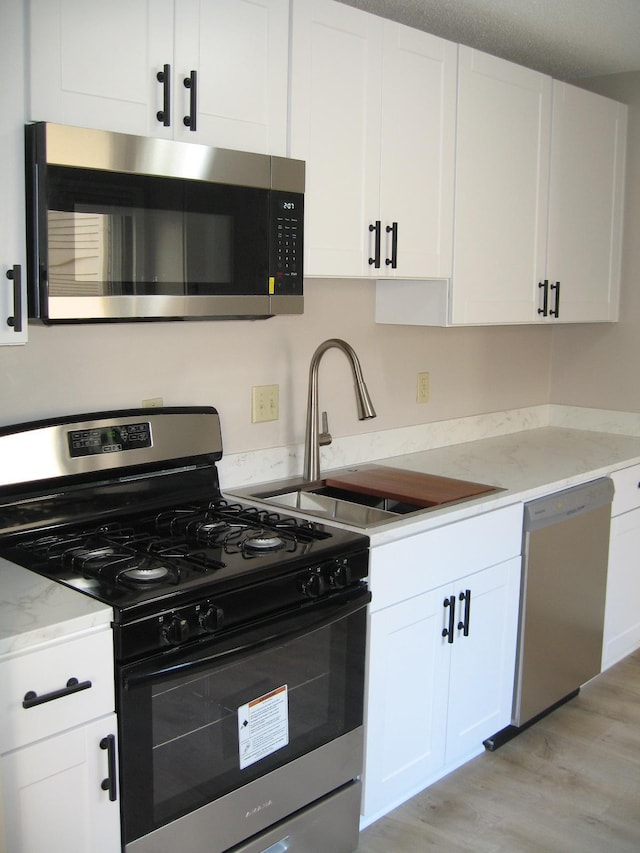 kitchen with stainless steel appliances, a sink, white cabinetry, light wood-style floors, and light stone countertops