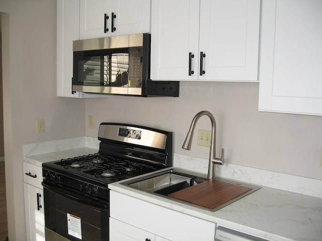 kitchen with stainless steel microwave, white cabinets, a sink, and gas stove