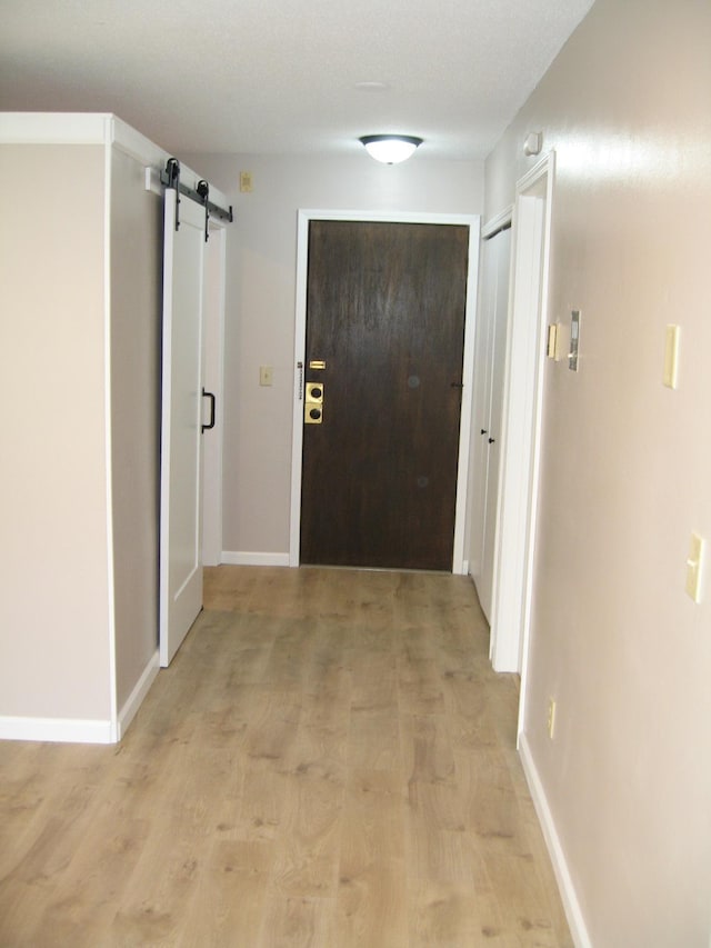 hallway featuring light wood-style floors, baseboards, and a barn door