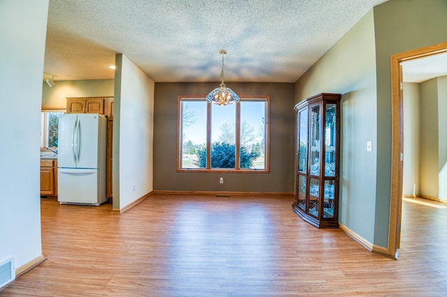 unfurnished dining area with light wood-style flooring, baseboards, and a textured ceiling