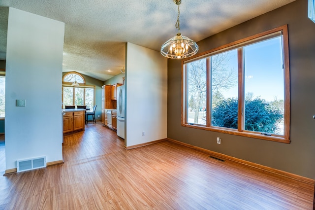 kitchen featuring freestanding refrigerator, brown cabinetry, visible vents, and light wood-style floors