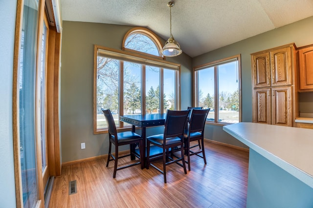 dining room with visible vents, light wood-style floors, vaulted ceiling, a textured ceiling, and baseboards