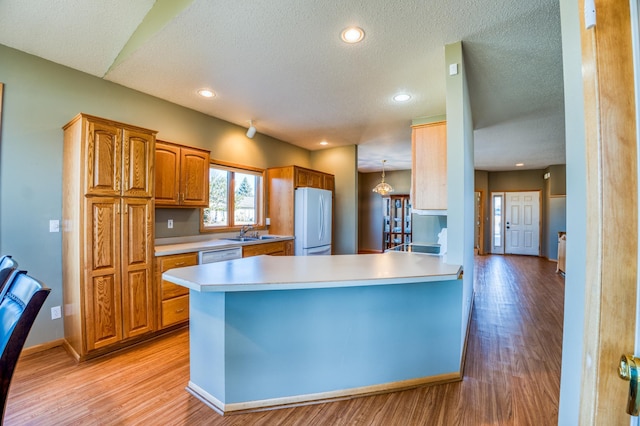 kitchen with white appliances, brown cabinetry, a peninsula, light countertops, and light wood-type flooring