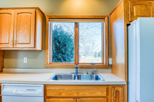 kitchen with white appliances, light countertops, a sink, and brown cabinetry