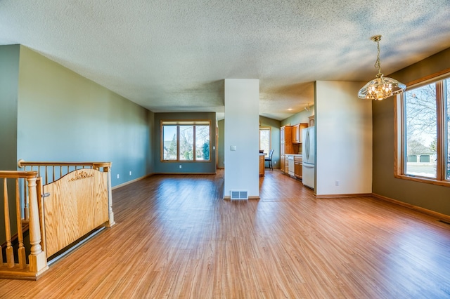 unfurnished living room featuring light wood finished floors, baseboards, visible vents, and a notable chandelier