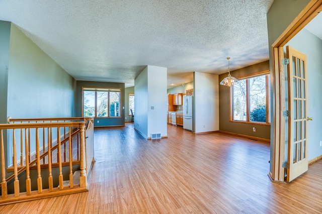 spare room with a notable chandelier, wood finished floors, visible vents, and a healthy amount of sunlight