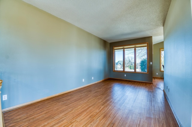 spare room with a textured ceiling, baseboards, and wood finished floors