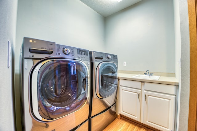 laundry room with light wood-type flooring, a sink, a textured ceiling, and separate washer and dryer