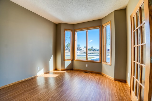 spare room with visible vents, baseboards, a textured ceiling, and light wood finished floors