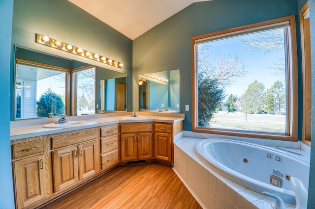 full bathroom with double vanity, lofted ceiling, a sink, wood finished floors, and a jetted tub