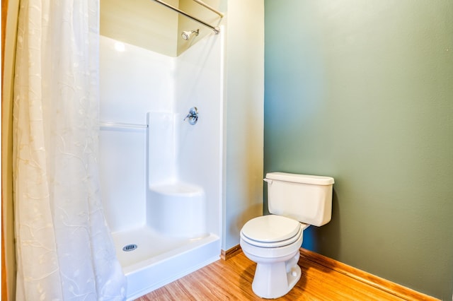 bathroom with baseboards, wood finished floors, toilet, and a shower with curtain