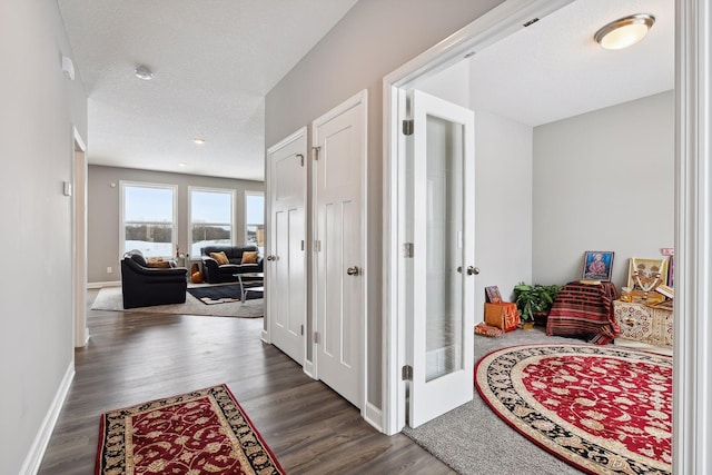 corridor featuring a textured ceiling, baseboards, and wood finished floors