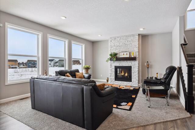 living area featuring a textured ceiling, a fireplace, wood finished floors, baseboards, and stairway