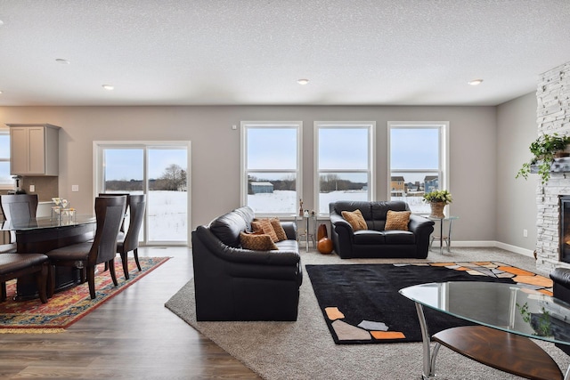 living area with baseboards, a fireplace, a textured ceiling, and light wood finished floors