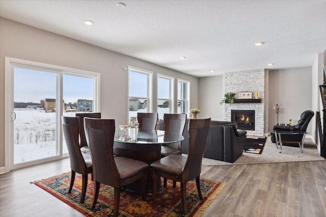 dining area with recessed lighting, light wood-style flooring, a textured ceiling, and a stone fireplace