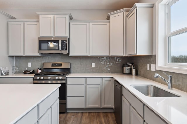 kitchen featuring stainless steel appliances, dark wood-style flooring, a sink, light countertops, and backsplash