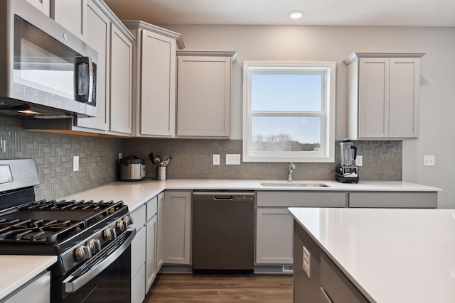 kitchen featuring dark wood-style flooring, light countertops, backsplash, appliances with stainless steel finishes, and a sink