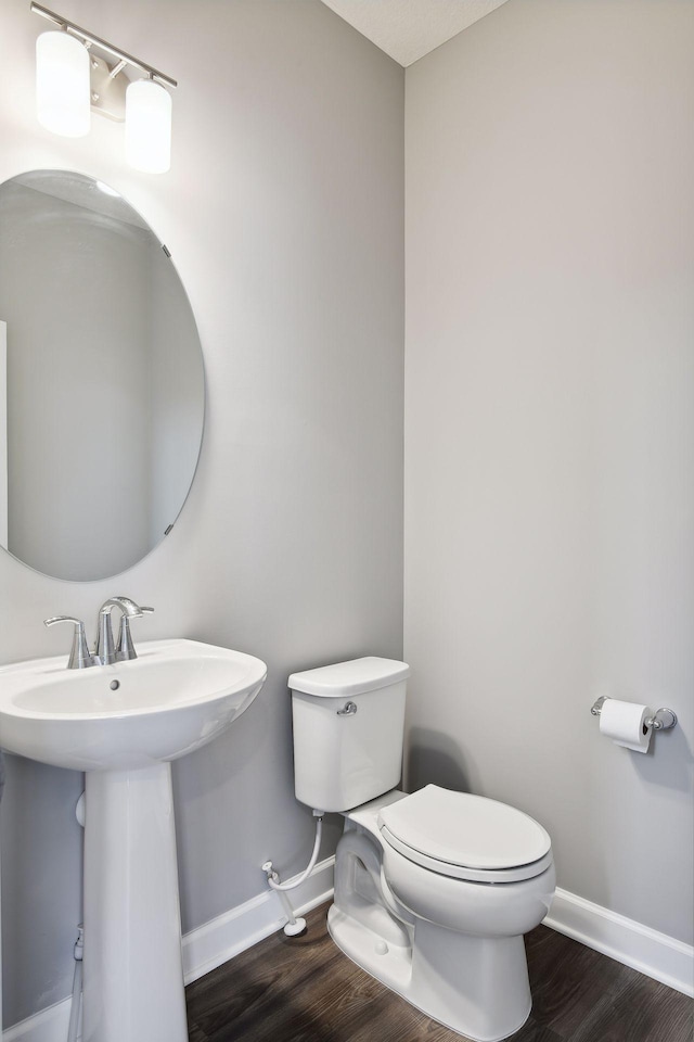 bathroom featuring toilet, a sink, baseboards, and wood finished floors