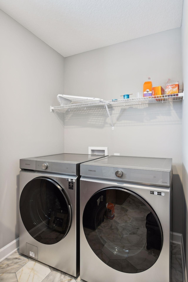 clothes washing area with a textured ceiling, laundry area, separate washer and dryer, baseboards, and marble finish floor