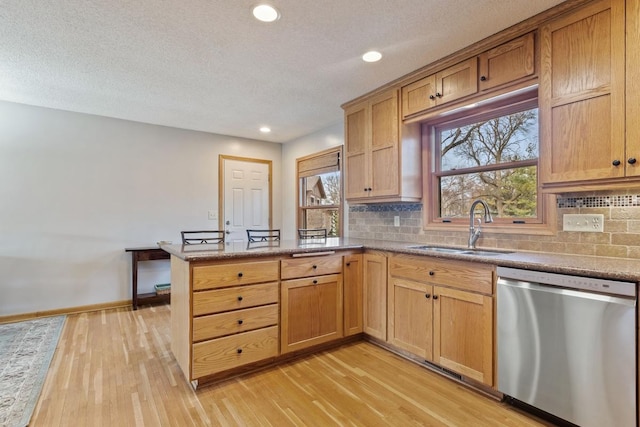 kitchen featuring a peninsula, a sink, light wood-type flooring, dishwasher, and tasteful backsplash