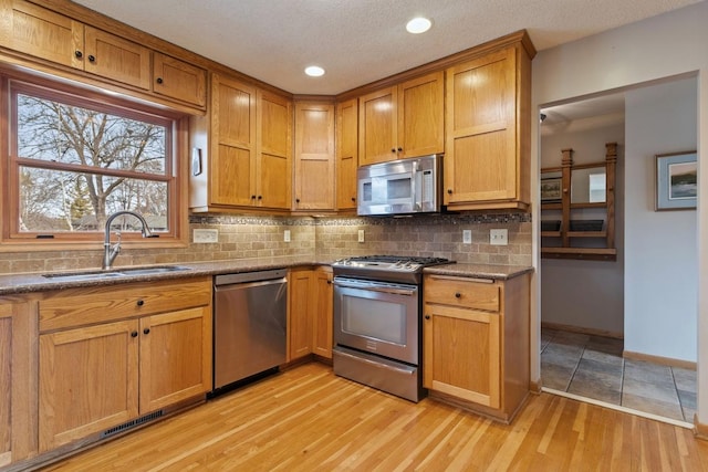 kitchen featuring tasteful backsplash, appliances with stainless steel finishes, a sink, light wood-type flooring, and baseboards