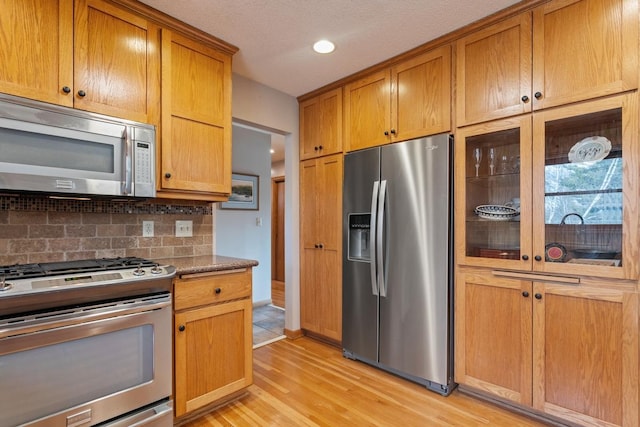 kitchen with light wood finished floors, tasteful backsplash, brown cabinetry, stainless steel appliances, and recessed lighting