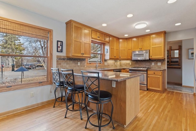 kitchen with a breakfast bar area, stainless steel appliances, a peninsula, a sink, and decorative backsplash