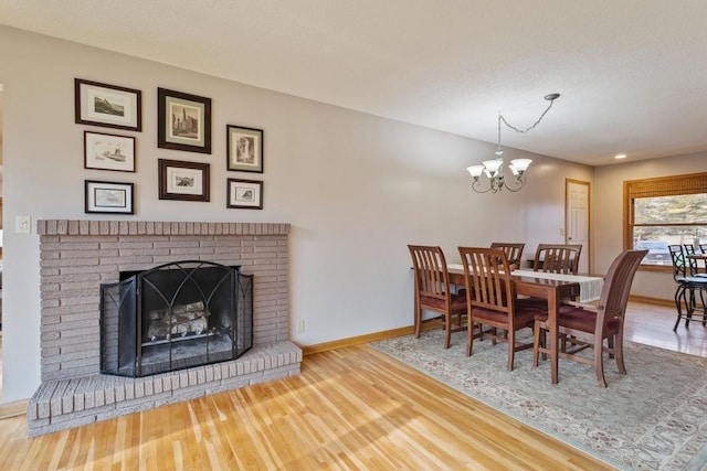 dining area featuring a chandelier, a fireplace, wood finished floors, and baseboards