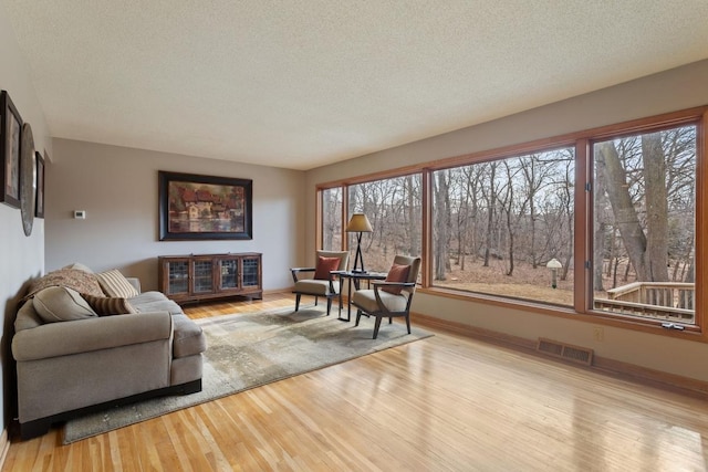 living area with visible vents, a textured ceiling, baseboards, and wood finished floors