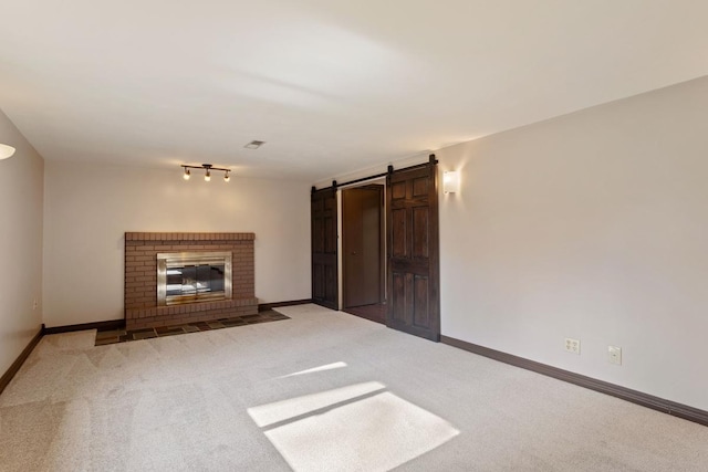 unfurnished living room featuring carpet floors, a barn door, a fireplace, and baseboards