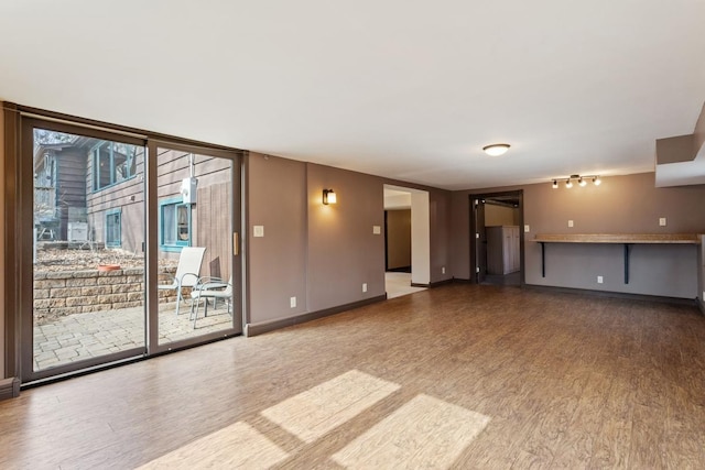 unfurnished living room featuring expansive windows, wood finished floors, and baseboards