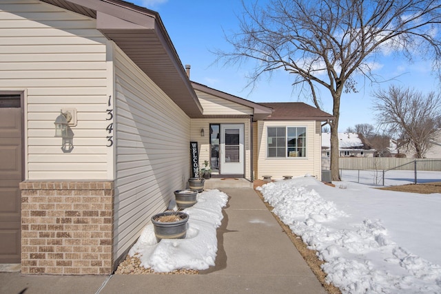 snow covered property entrance with brick siding, a garage, and fence