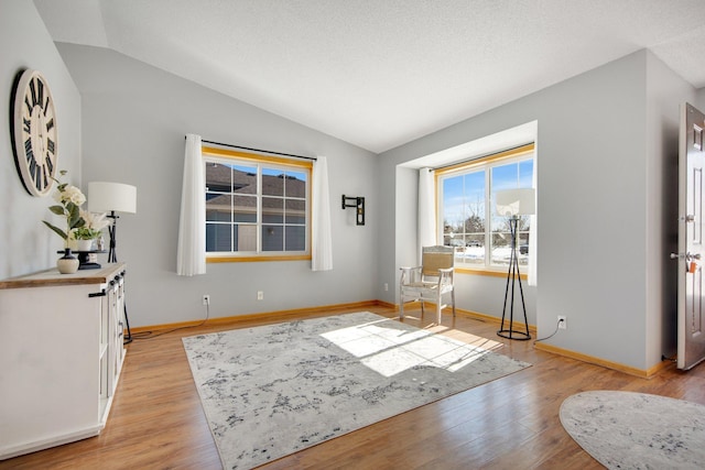 unfurnished room with baseboards, lofted ceiling, a textured ceiling, and light wood-style flooring