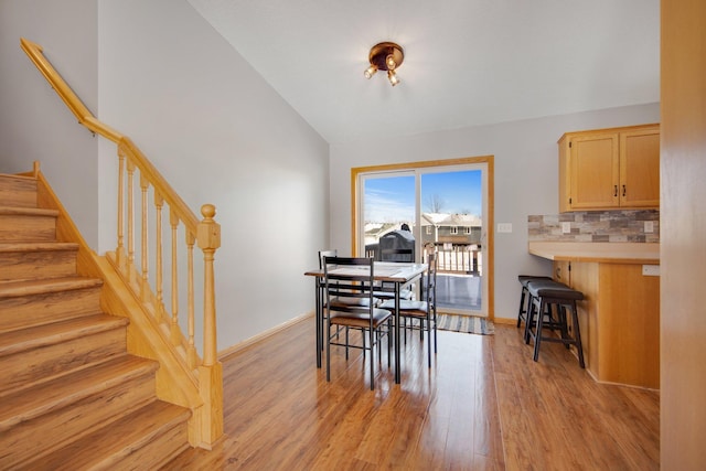 dining area featuring light wood finished floors, stairway, baseboards, and vaulted ceiling