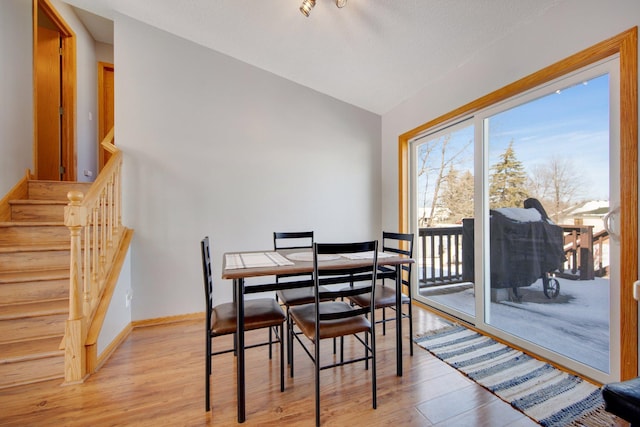 dining area featuring light wood-style flooring, baseboards, stairs, and lofted ceiling