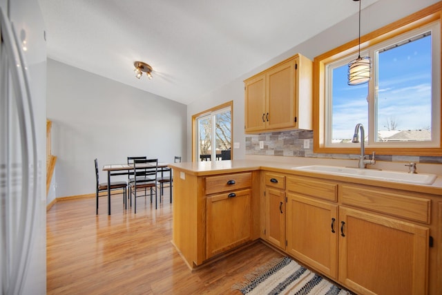 kitchen with light countertops, lofted ceiling, a peninsula, freestanding refrigerator, and a sink