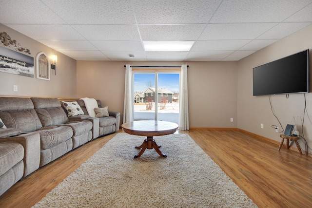 living room featuring a drop ceiling, light wood-style flooring, and baseboards