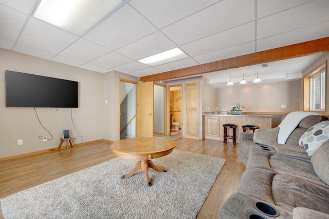 living area featuring a drop ceiling, light wood-type flooring, and baseboards