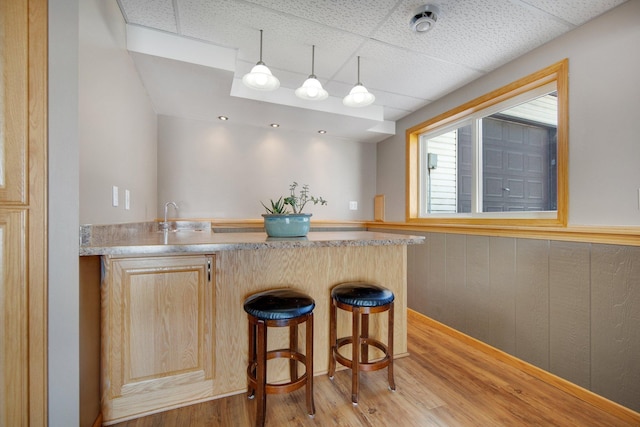 kitchen featuring light brown cabinetry, light wood-style floors, a peninsula, light countertops, and a paneled ceiling