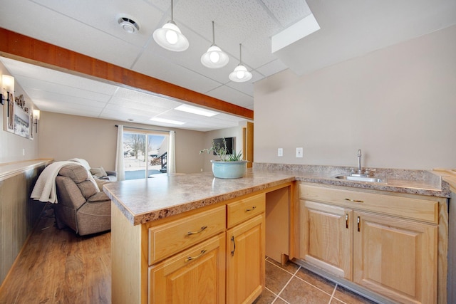 kitchen featuring light brown cabinets, a sink, light countertops, a paneled ceiling, and open floor plan