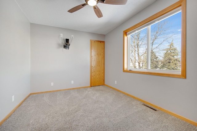 carpeted spare room featuring ceiling fan, visible vents, baseboards, and a textured ceiling